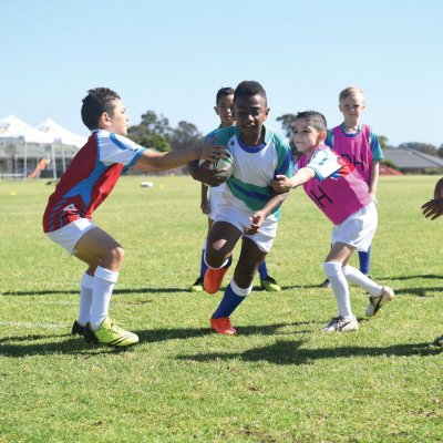 Young boys on a field playing rugby league, with a player being tackled